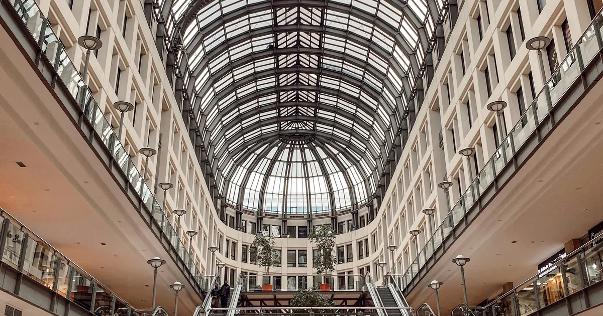 Interior de un centro comercial con zonas de paso y accesos a tiendas.